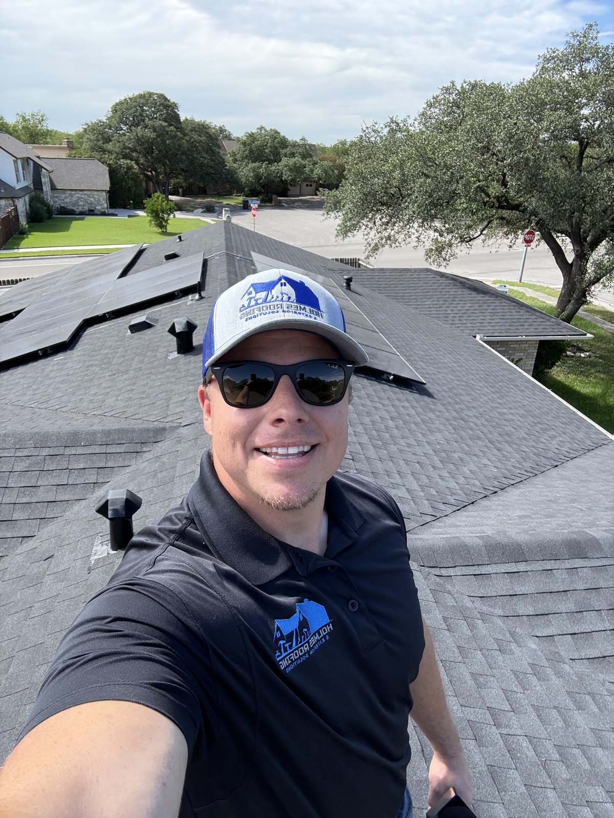 Joshua Holmes smiling on a finished rooftop, wearing branded Holmes Roofing gear