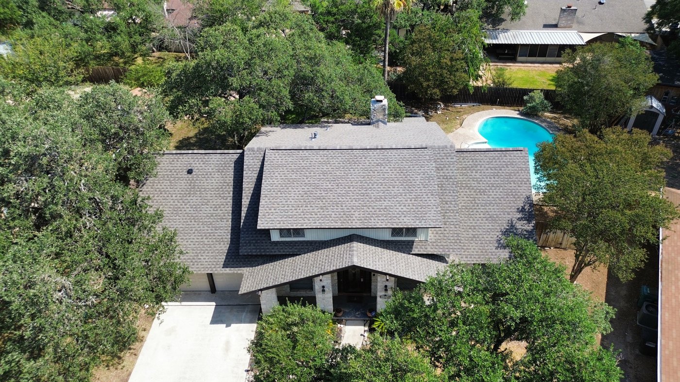 Completed roof replacement, red-brick San Antonio-area home with a pool and mature trees, aerial view