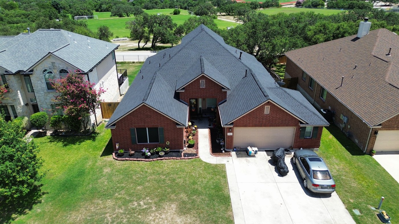 Aerial view of a finished roof replacement, red-brick home with mature trees