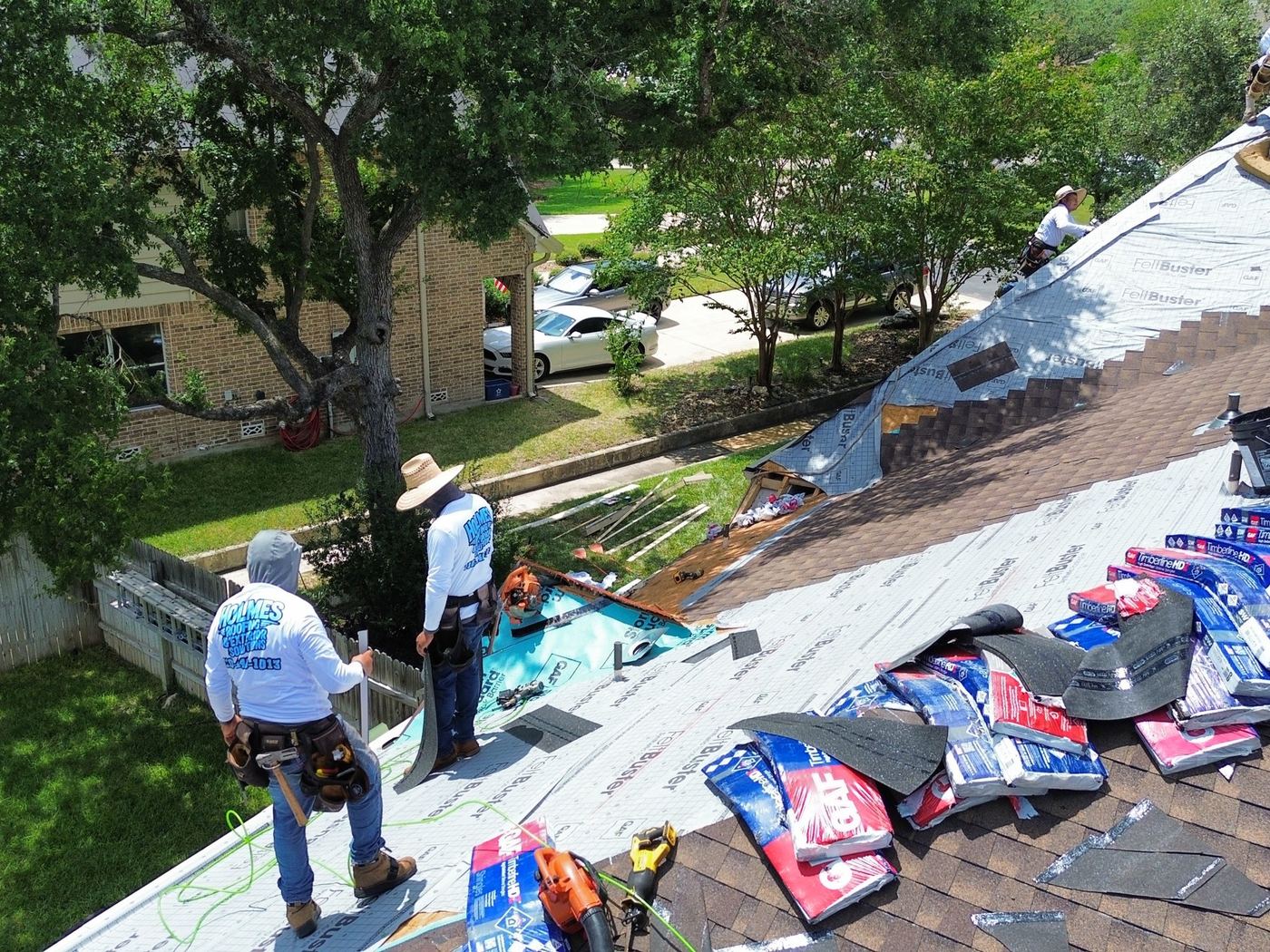 Aerial view of a Holmes Roofing crew mid-tear-off, underlayment and shingle bundles staged on the roof