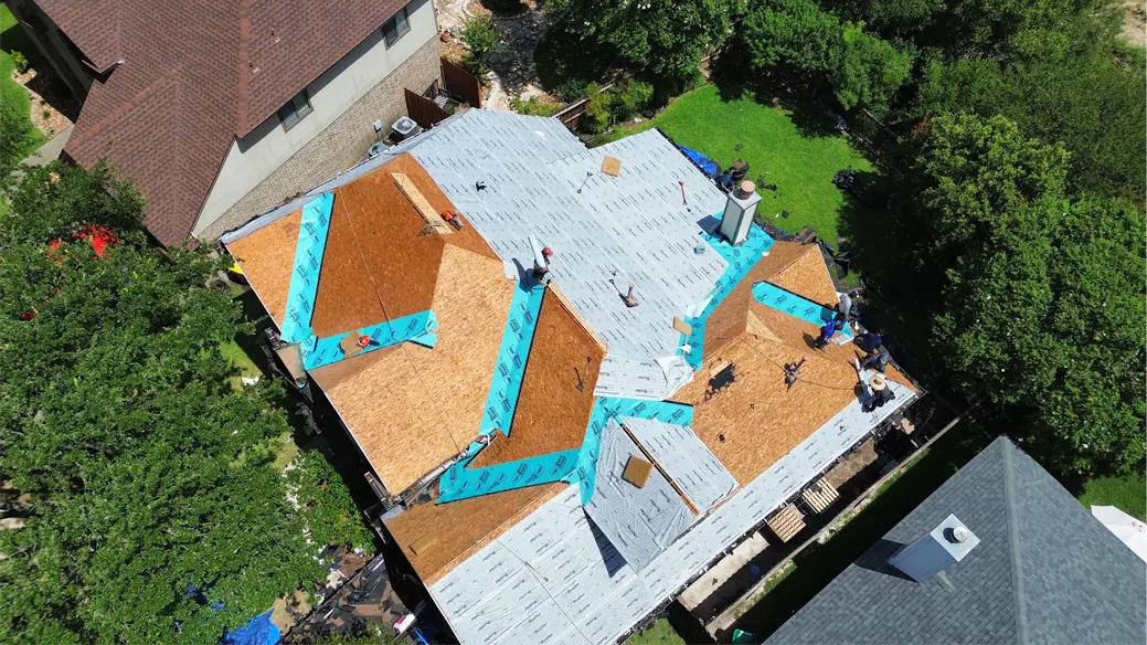 Aerial view of a roof with the decking and underlayment exposed, crew on site
