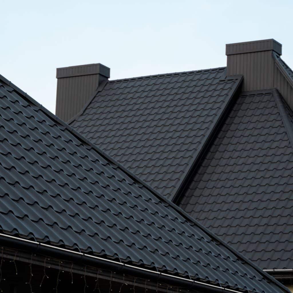 Black metal roof panels with a tiled texture, complemented by chimneys and a modern architectural design