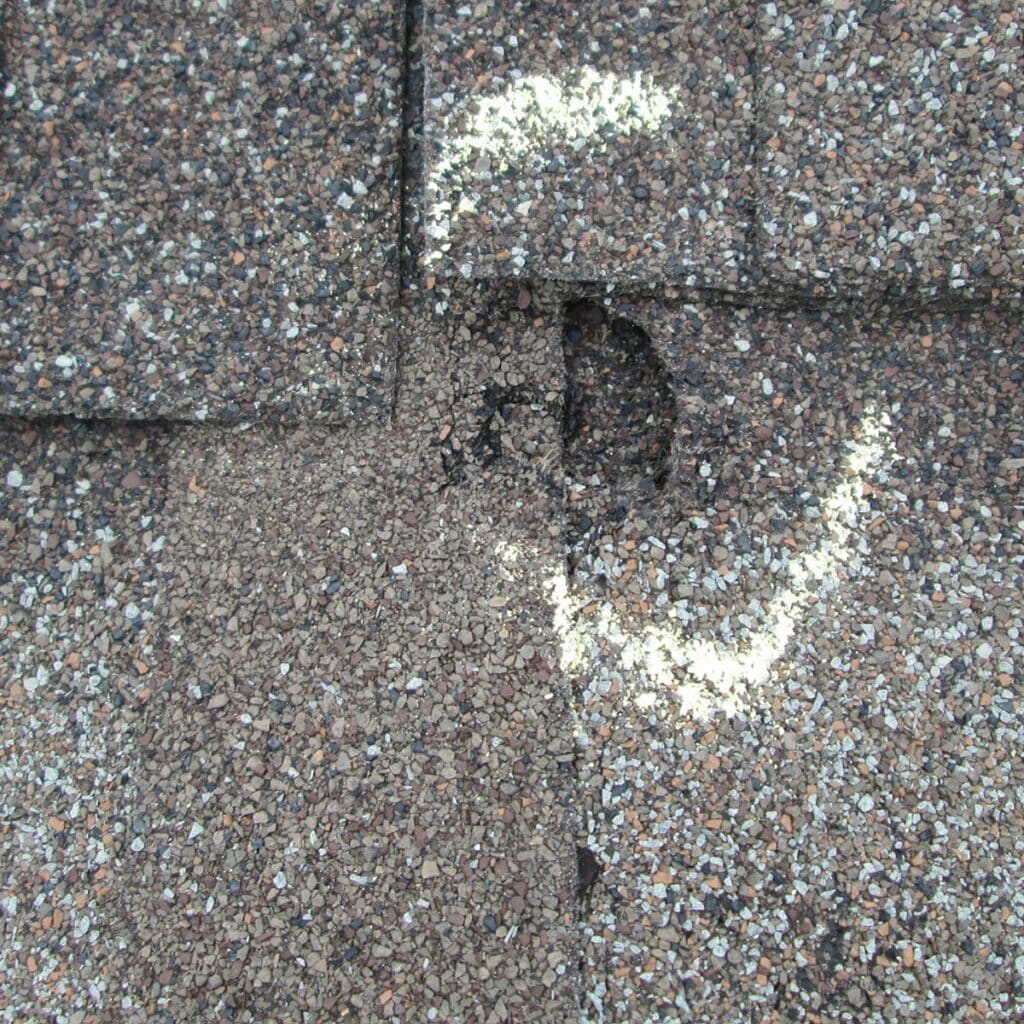 Close-up of a damaged asphalt shingle roof with visible holes marked for repair