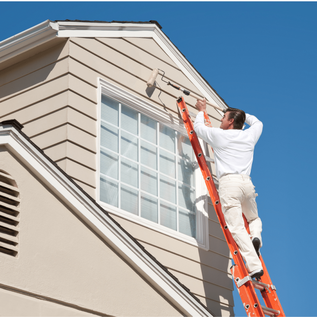 professional house painter standing on a ladder using a long roller to roll on paint to a home exterior