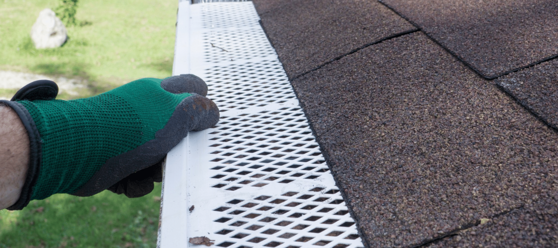 A gloved hand adjusting a white gutter guard on a roof to prevent debris accumulation