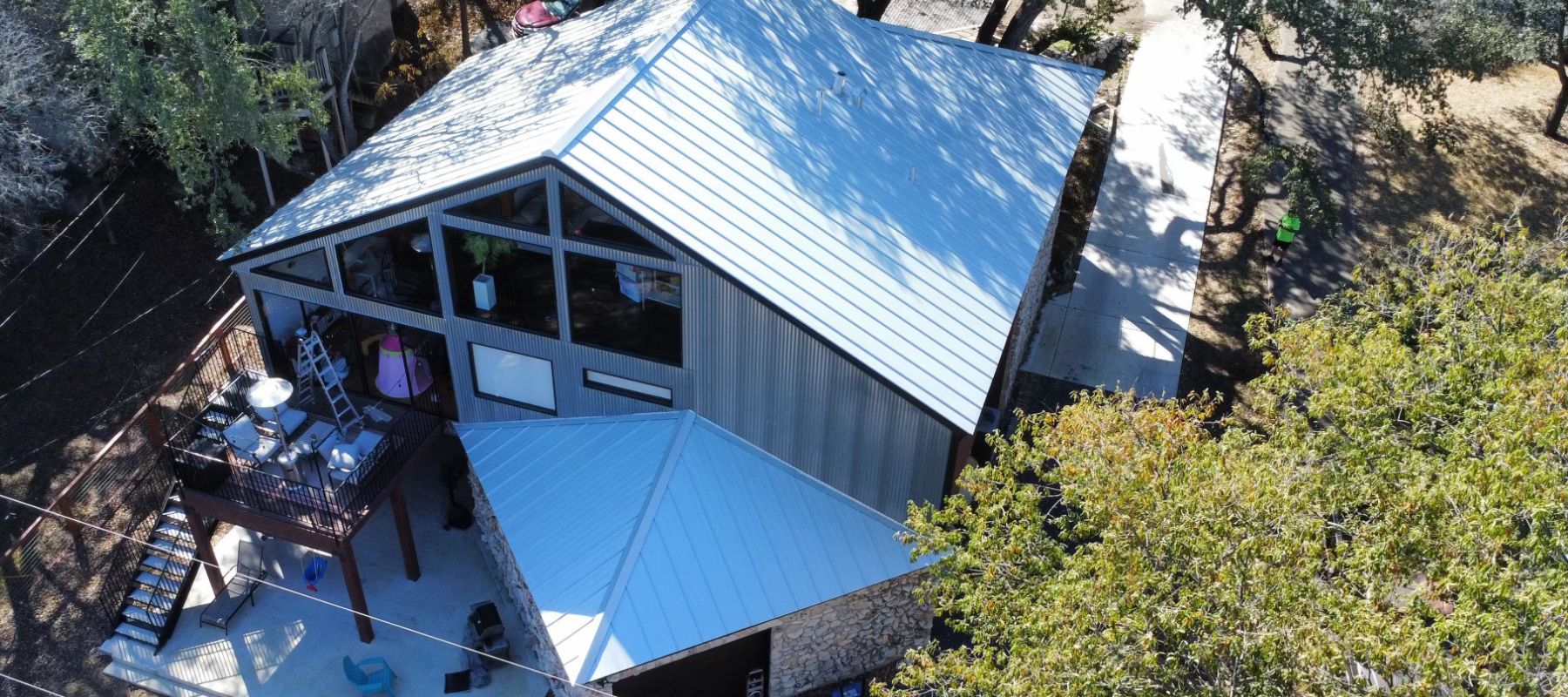 A modern home with a sleek metal roof, large glass windows, and an outdoor deck, nestled in a wooded area