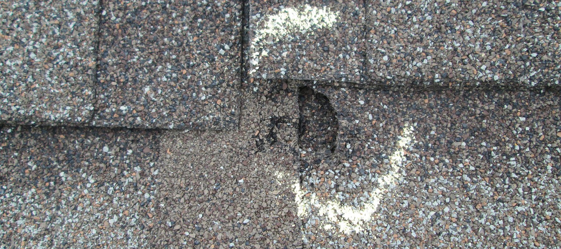 Close-up of a damaged asphalt shingle roof with visible holes marked for repair