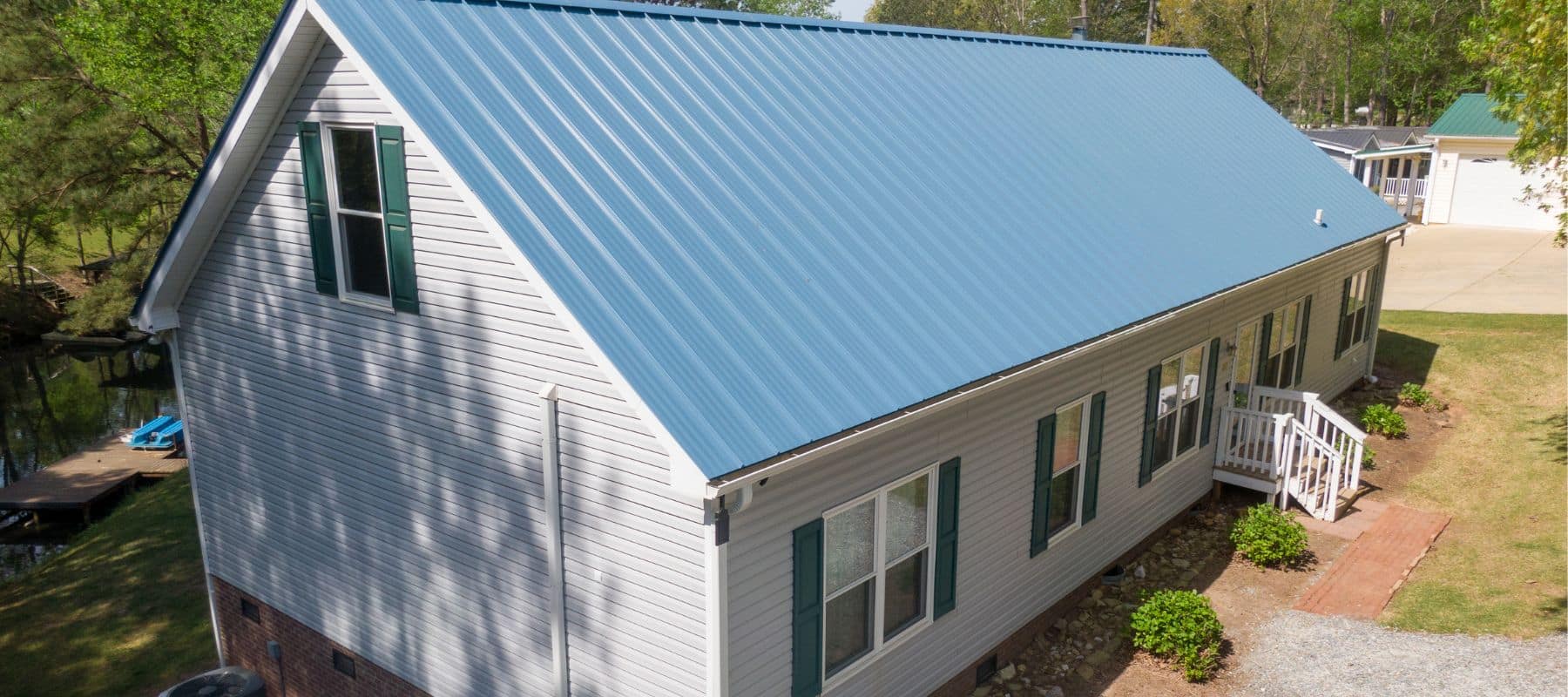 White house with a vibrant blue metal roof, surrounded by a well-maintained yard and trees