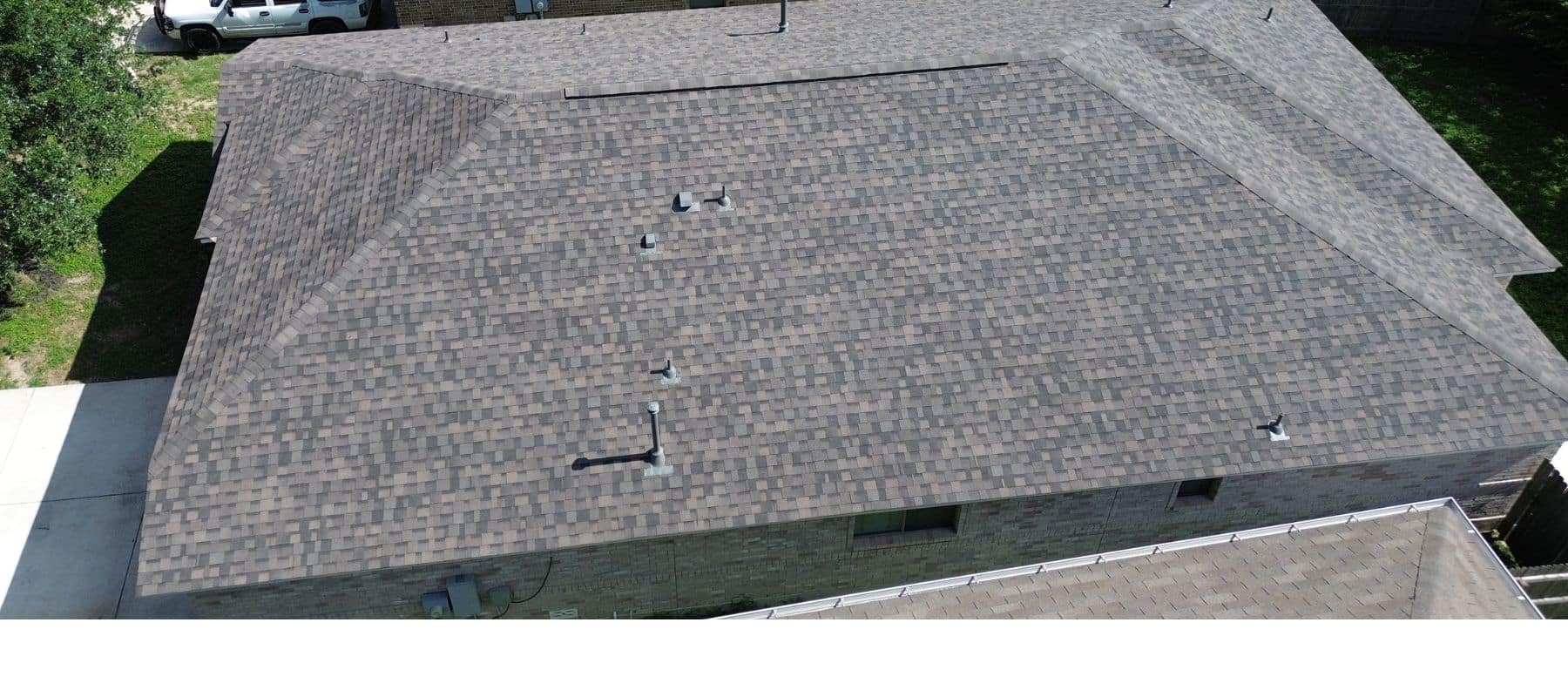 Aerial view of a house with a newly installed brown shingle roof, featuring multiple vents and a clean finish