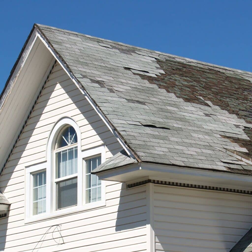 A home with severely weathered and missing shingles on the roof, indicating damage in need of repair