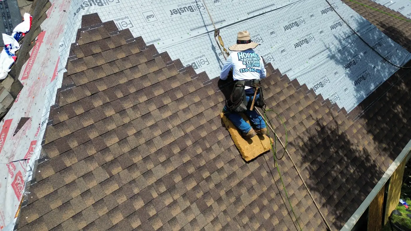 Holmes Roofing crew member in branded shirt installing architectural shingles over synthetic underlayment in Stone Oak, San Antonio, TX, July 2025